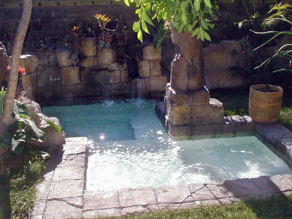 Tropical pool and spa with concrete rock walls and waterfall