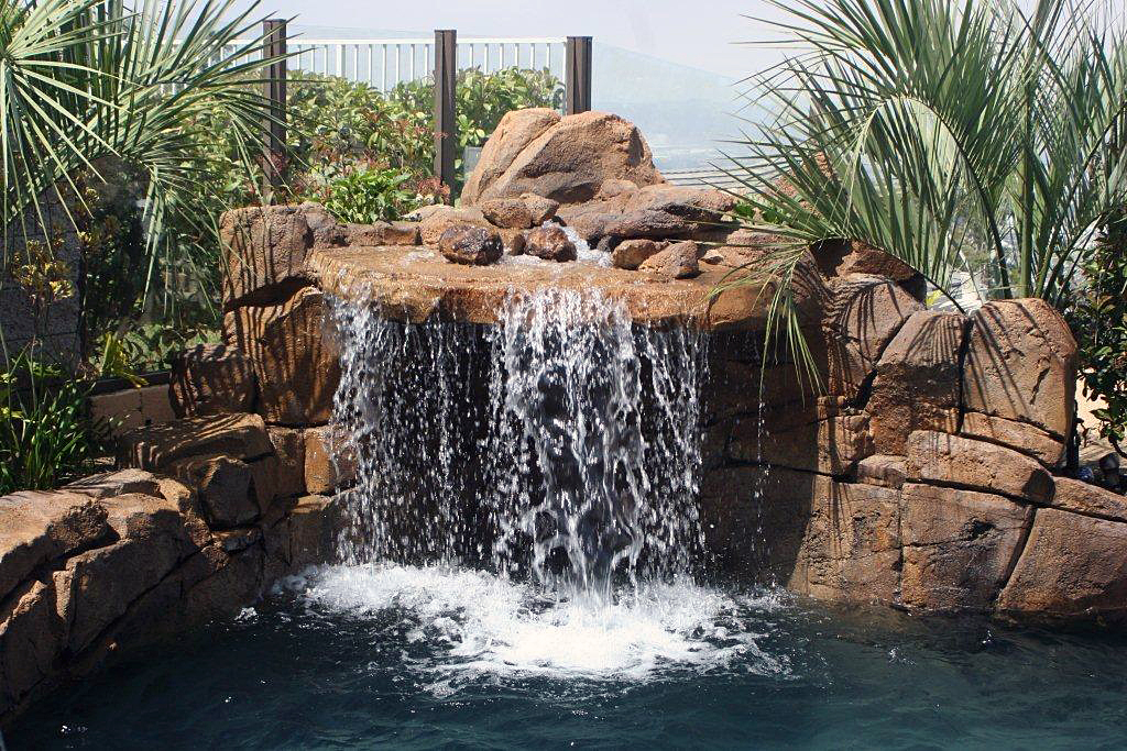 Poolside concrete rock waterfall cascading into blue pool