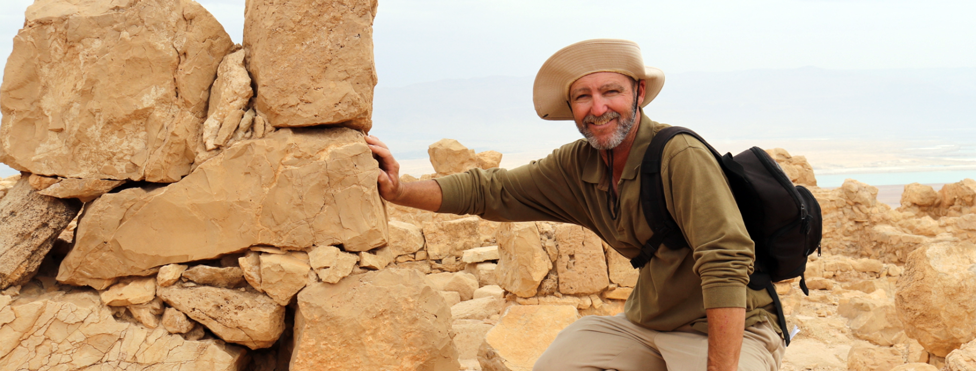 Richard posing by real rocks in the desert wearing a large hat and an olive-green shirt